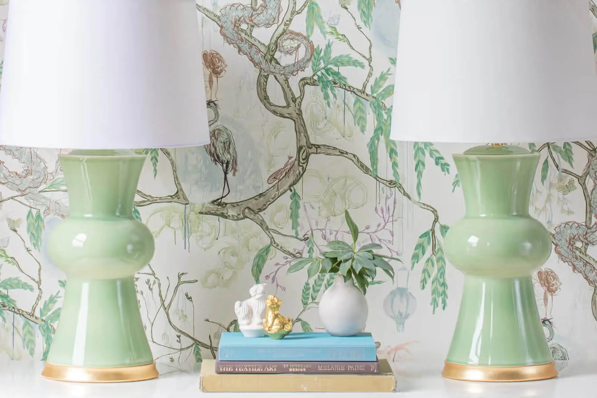 Two beautiful green Hwang Bishop lamps shot against a rich wallpaper.